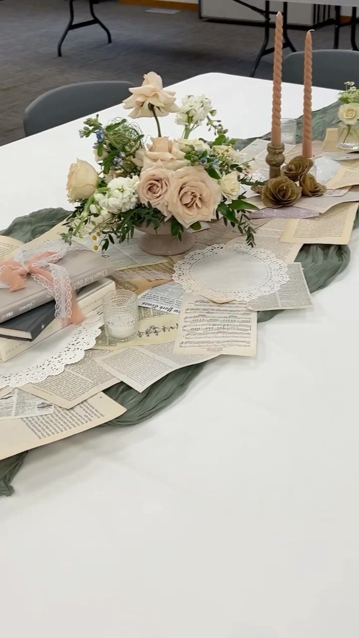 Vintage table setting with peach roses, old book pages, and tall taper candles.