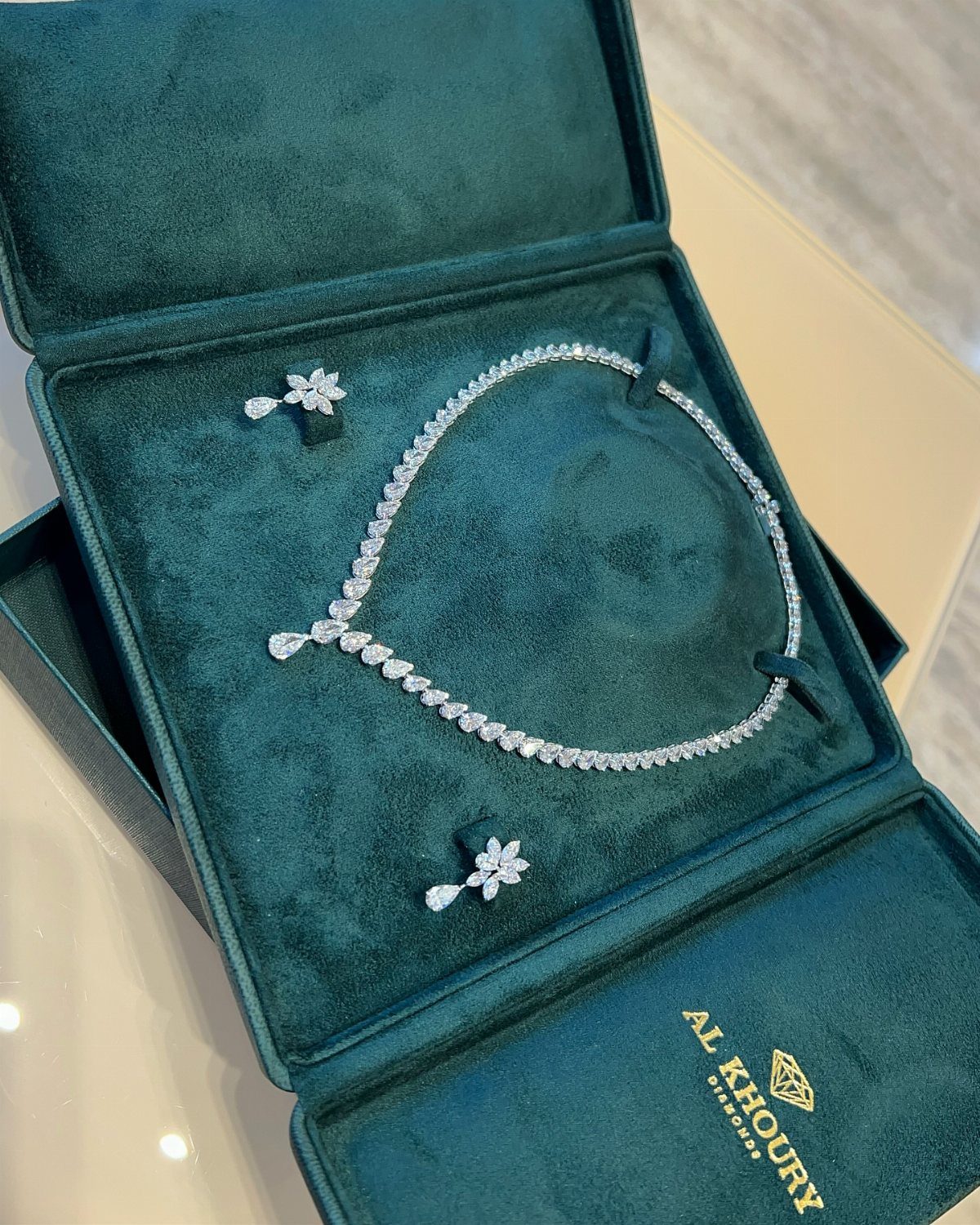 Diamond necklace and matching earrings displayed in a dark teal velvet jewelry box.