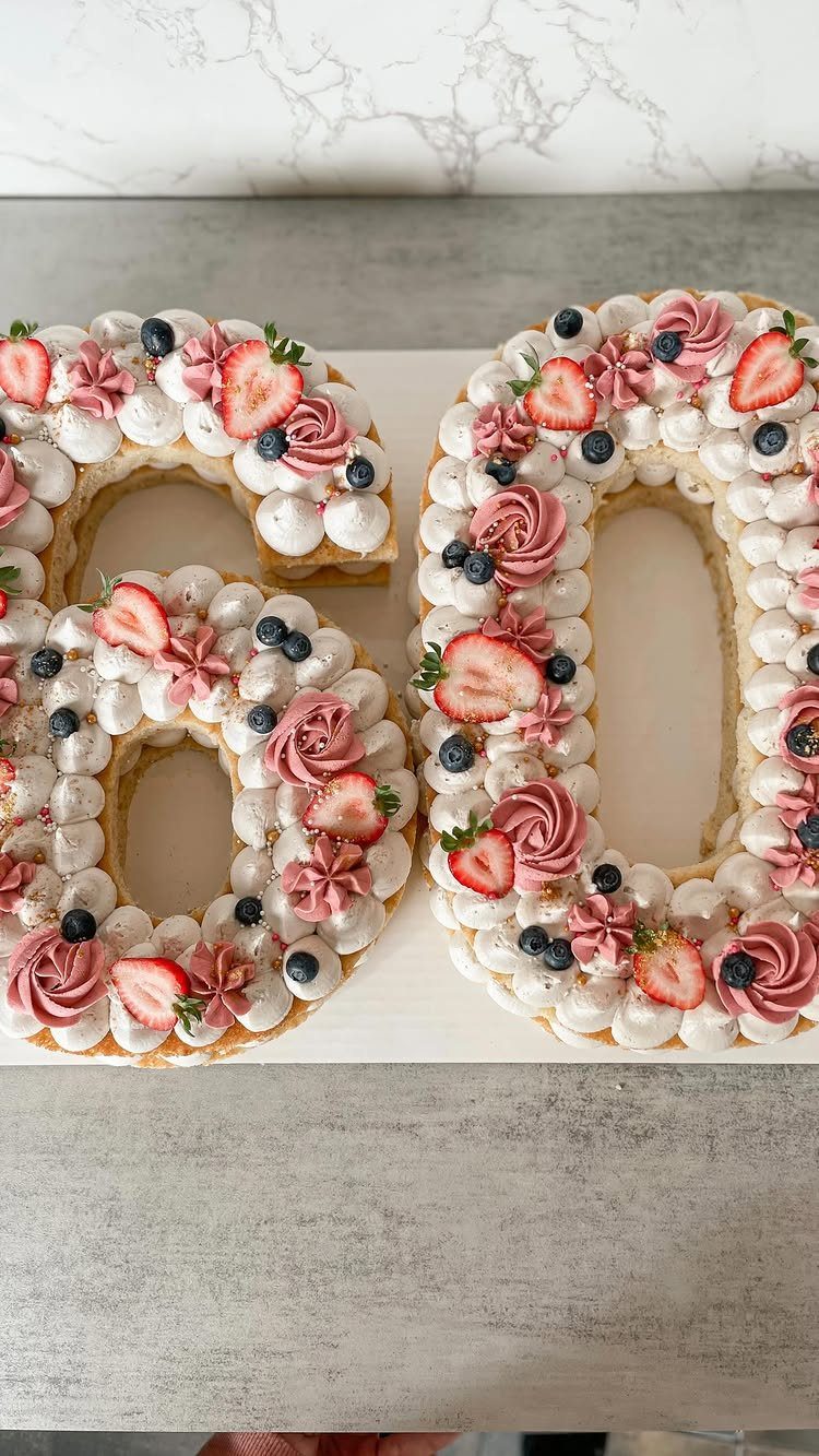 Number 60 cake decorated with white cream, pink roses, strawberries and blueberries.