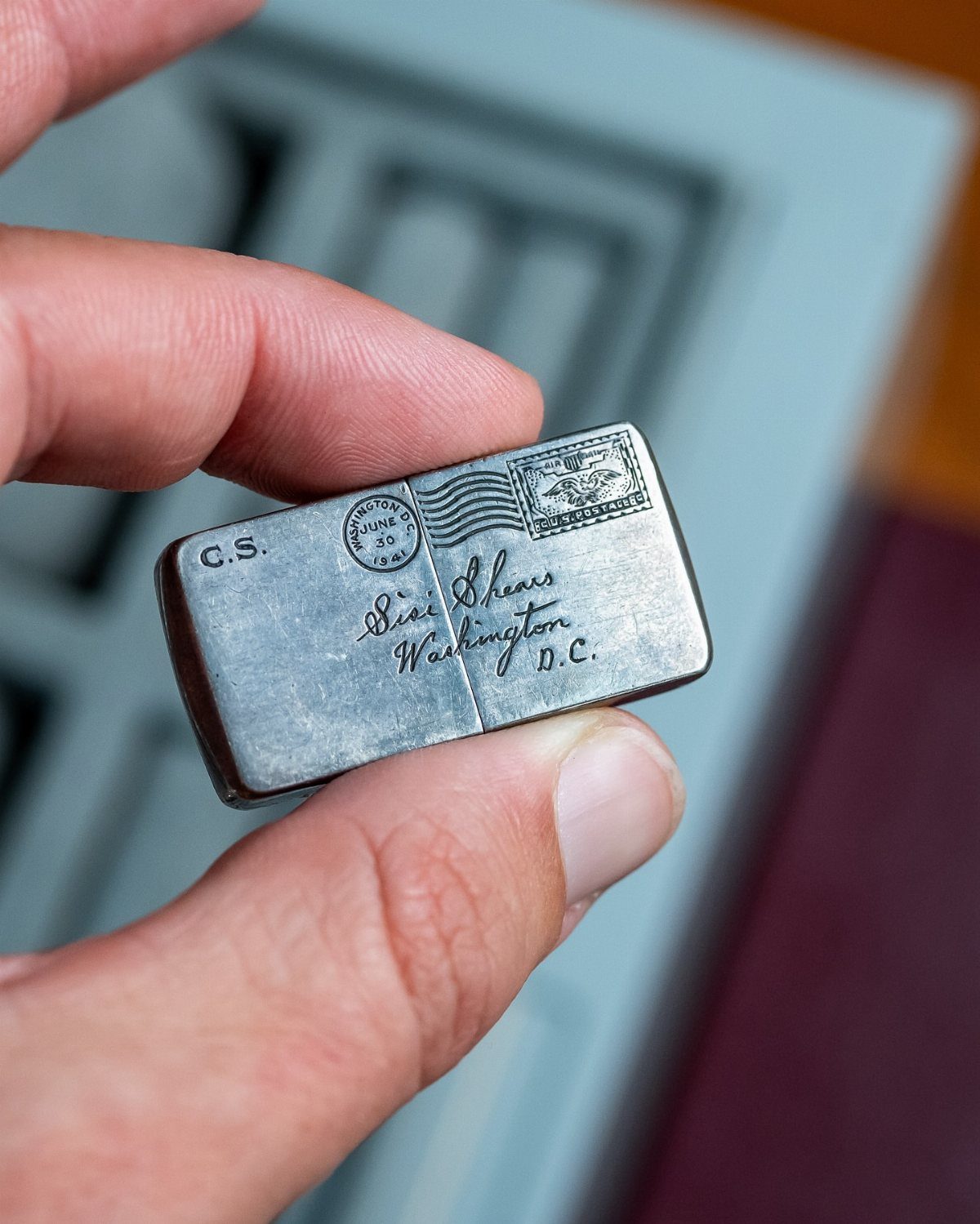 Small silver metal case with vintage postage engravings held between two fingers