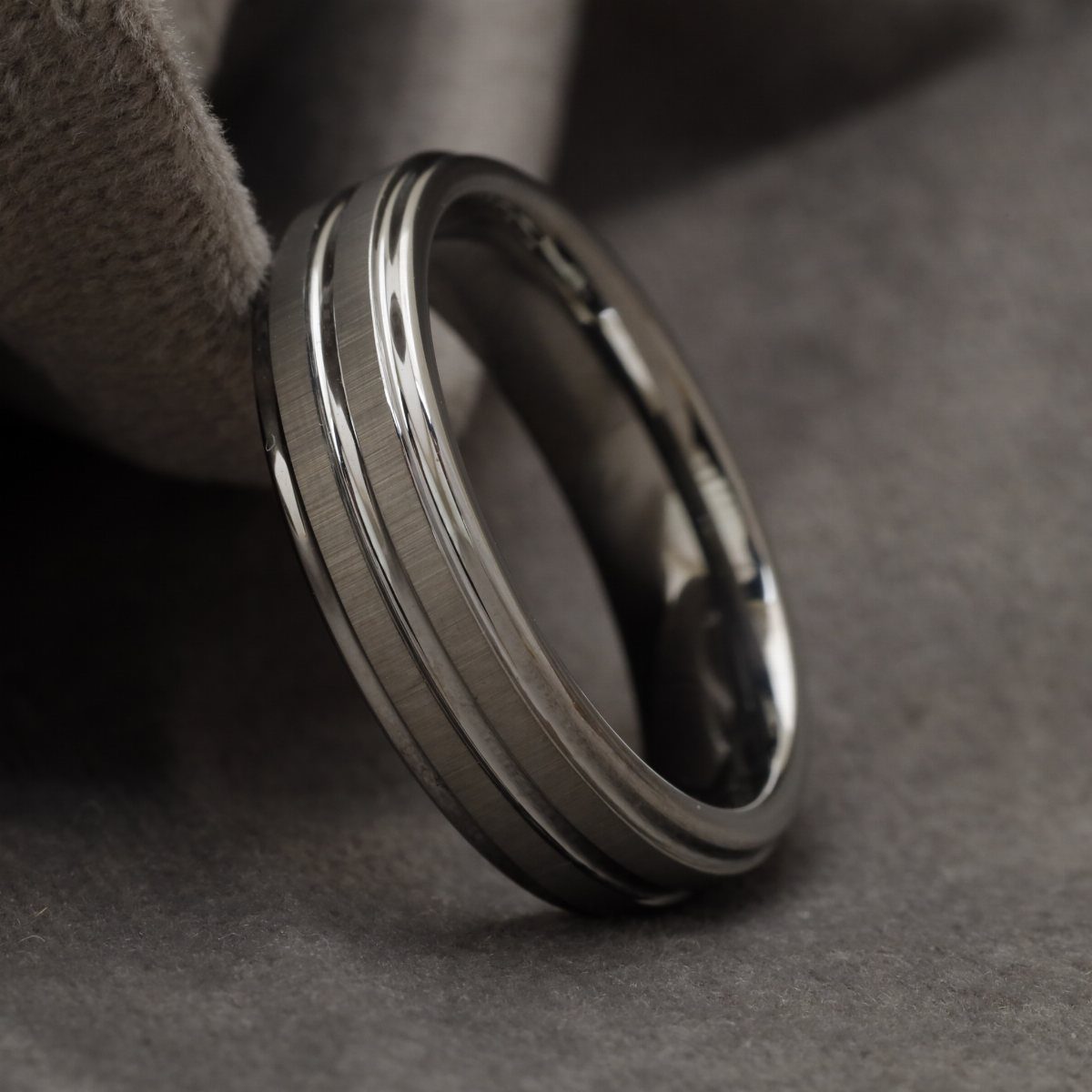 Grey tungsten ring with brushed finish and polished grooves on grey fabric