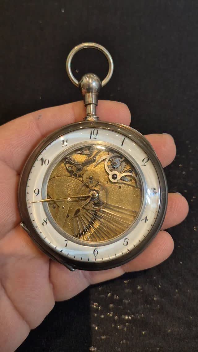 Silver pocket watch with visible gold internal gears held in a person's hand