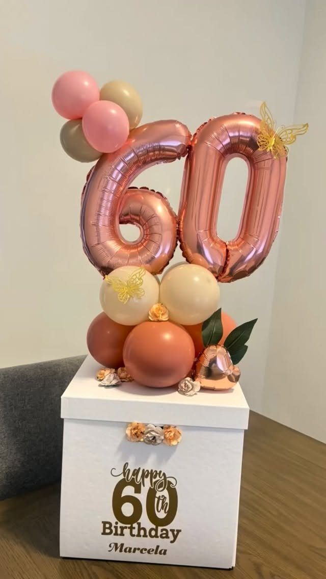 White 60th birthday gift box topped with rose gold number balloons and butterflies.