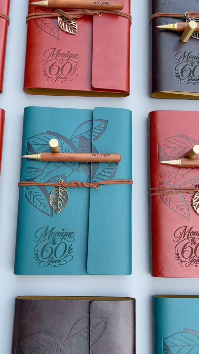 Leather-bound journals in red and teal embossed with Monique 60 Jaar text.