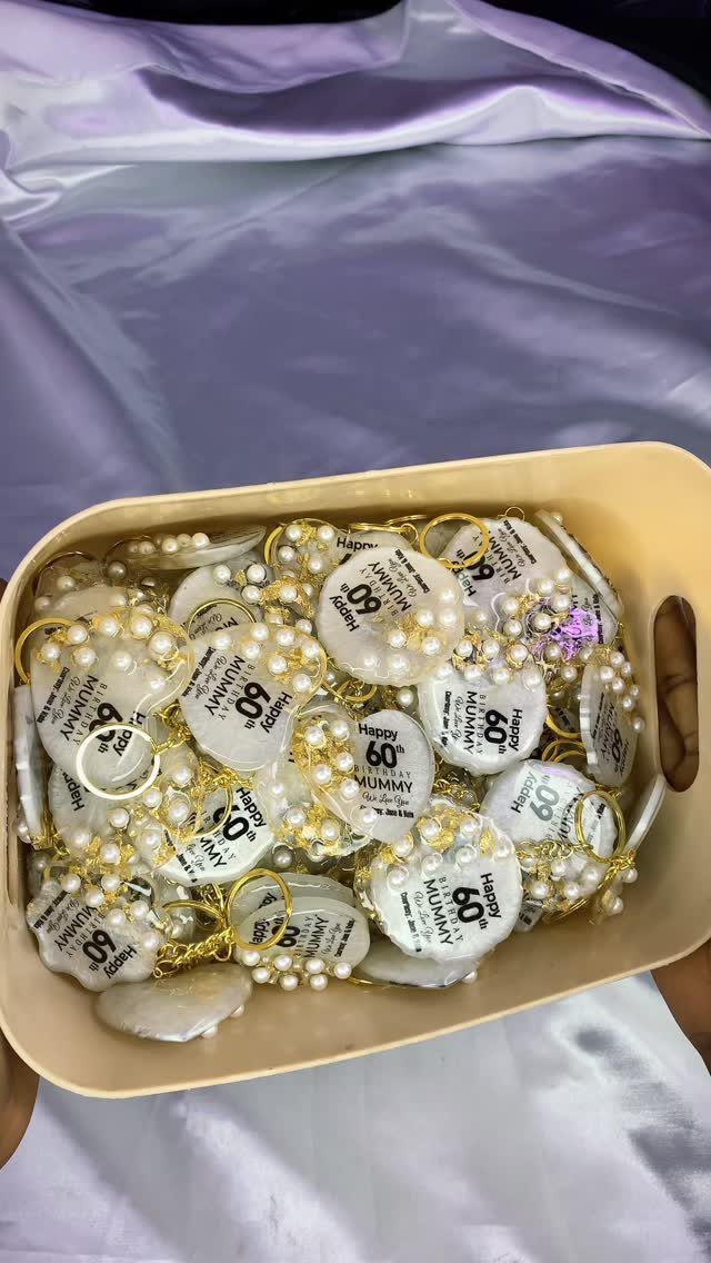 White 60th birthday badges with pearl chains in a beige tray on purple fabric