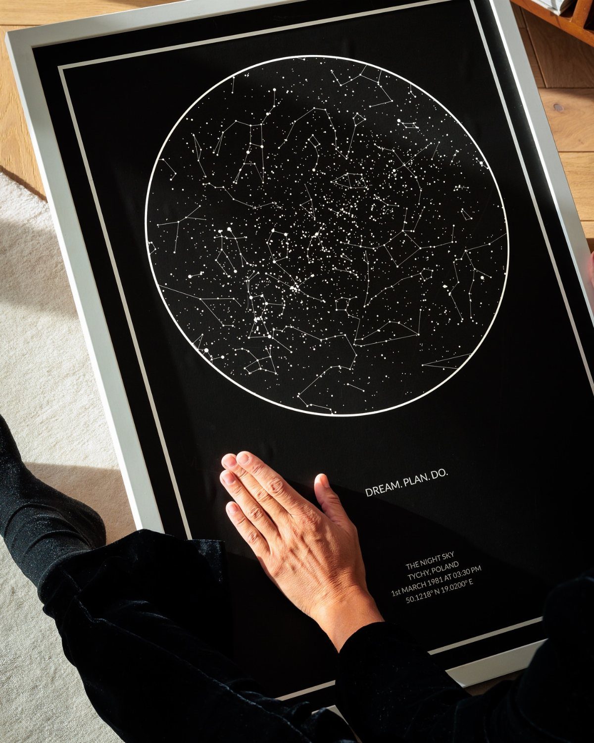 Framed black star map with white constellations and a hand touching the glass.