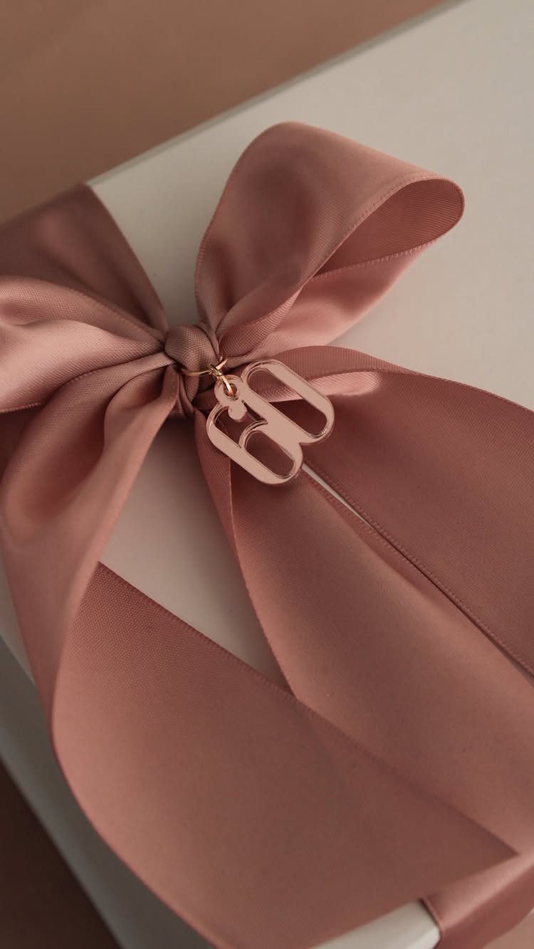 White gift box with a dusty rose satin ribbon and gold letter B charm