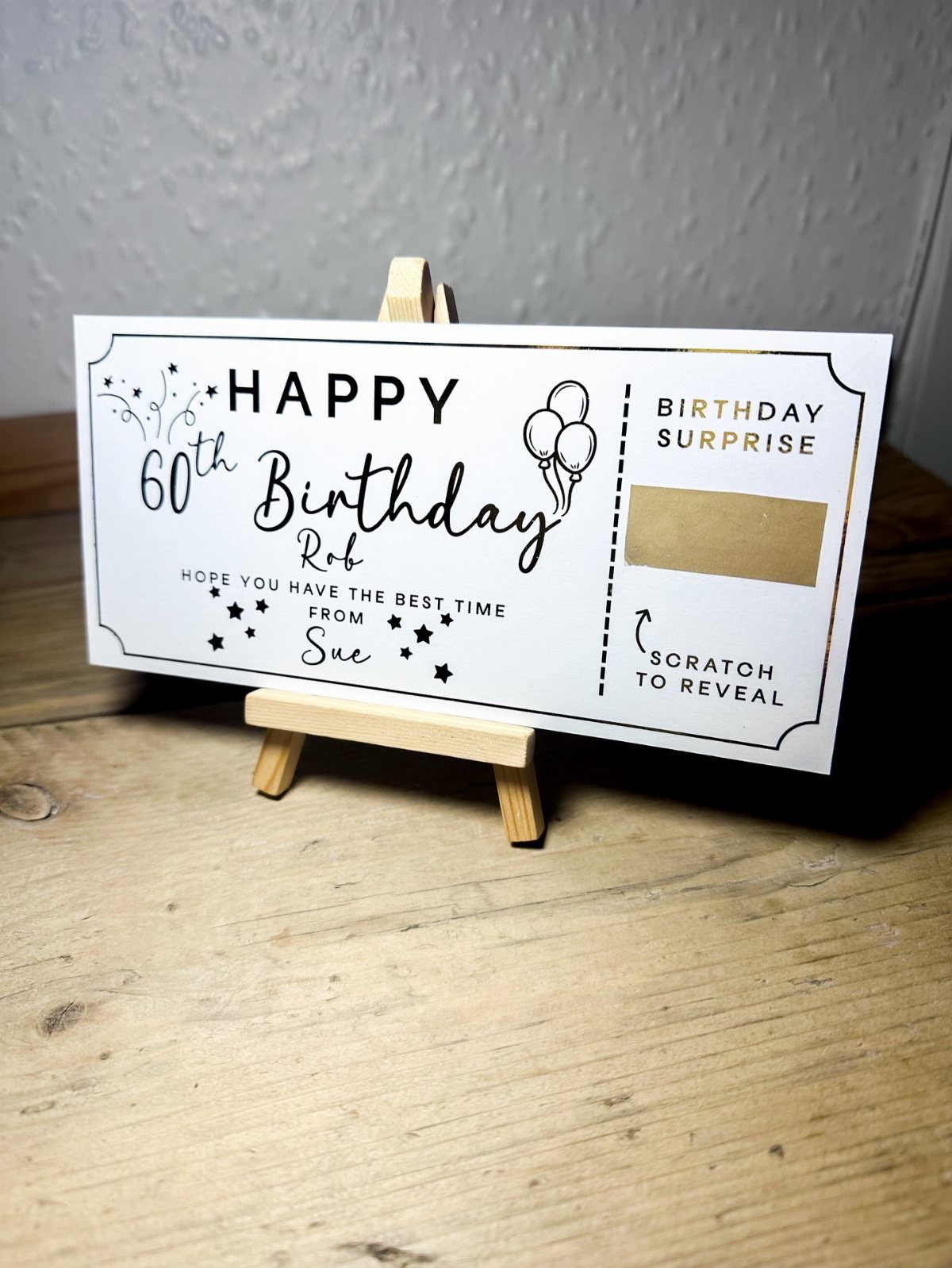 Scratch-off 60th birthday surprise card displayed on a small wooden easel.