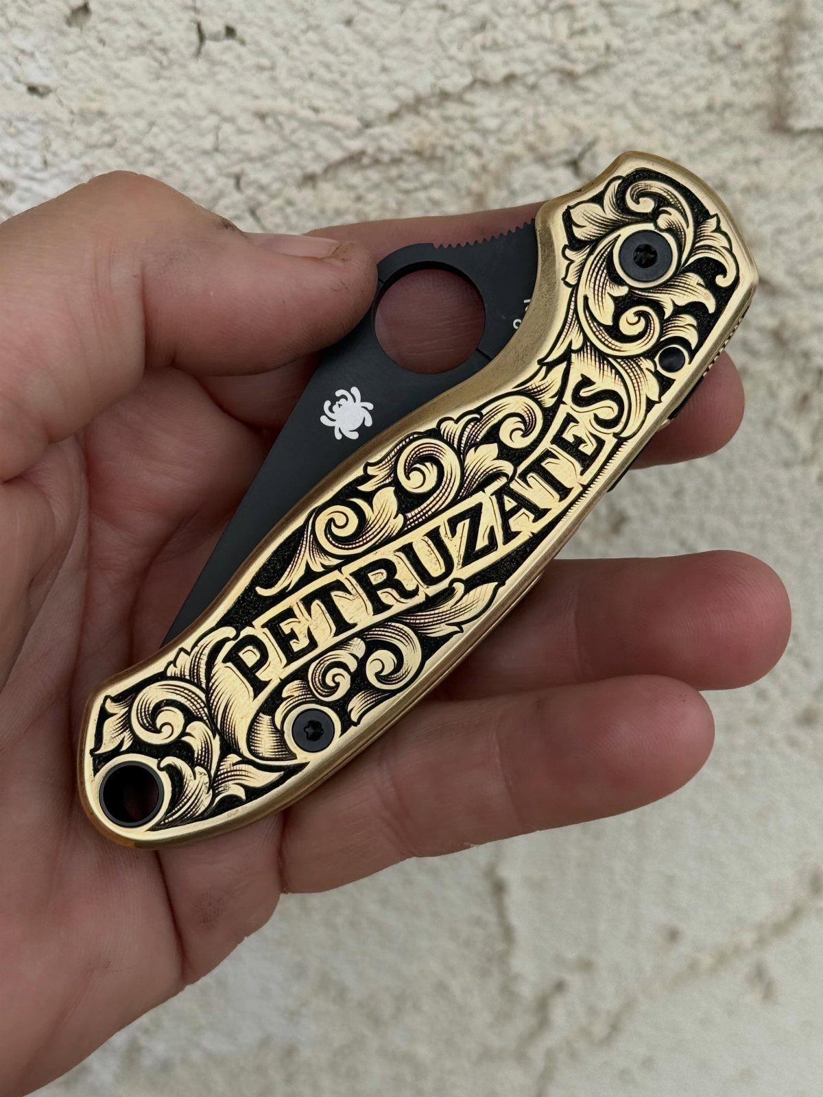 Engraved gold pocket knife with the name Petruzates held in a hand.