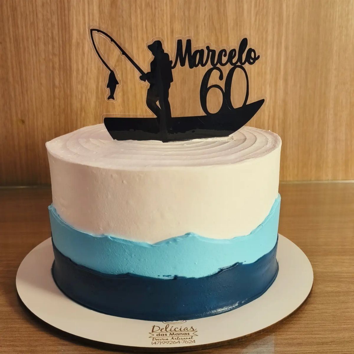 Fishing themed birthday cake with blue frosting and a silhouette fisherman topper.