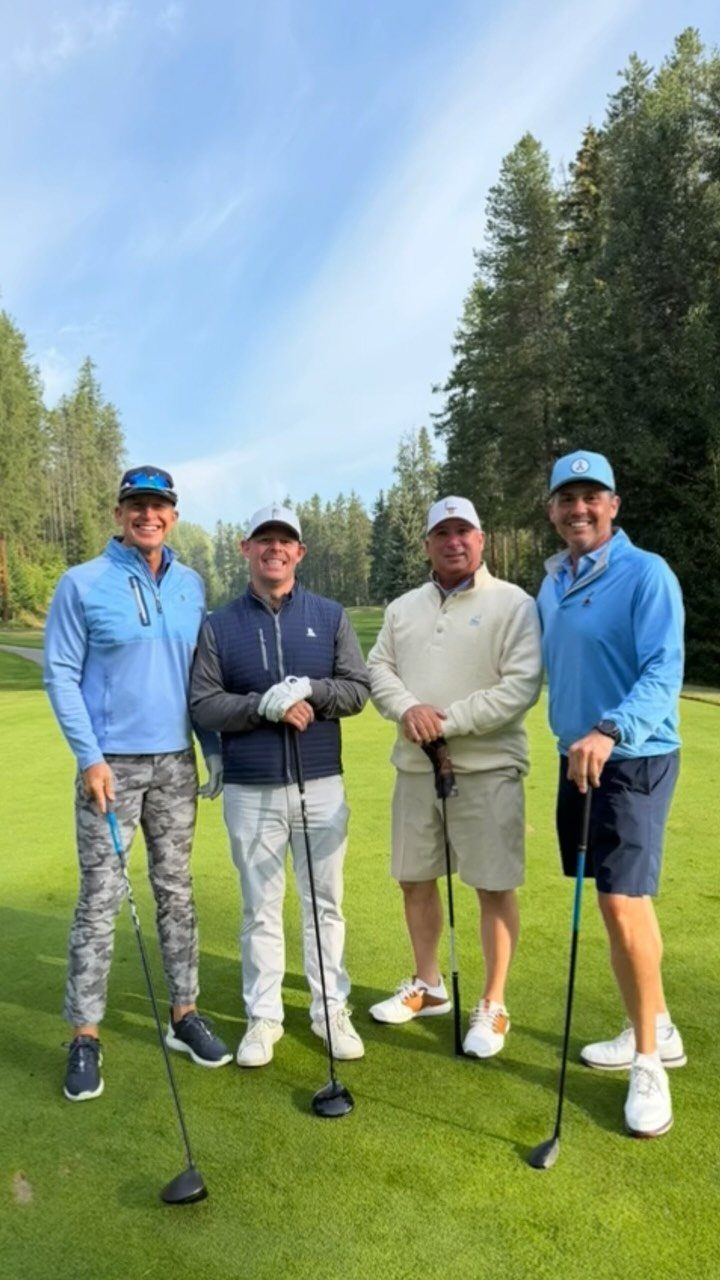 Four men in golf attire posing with clubs on a lush green golf course