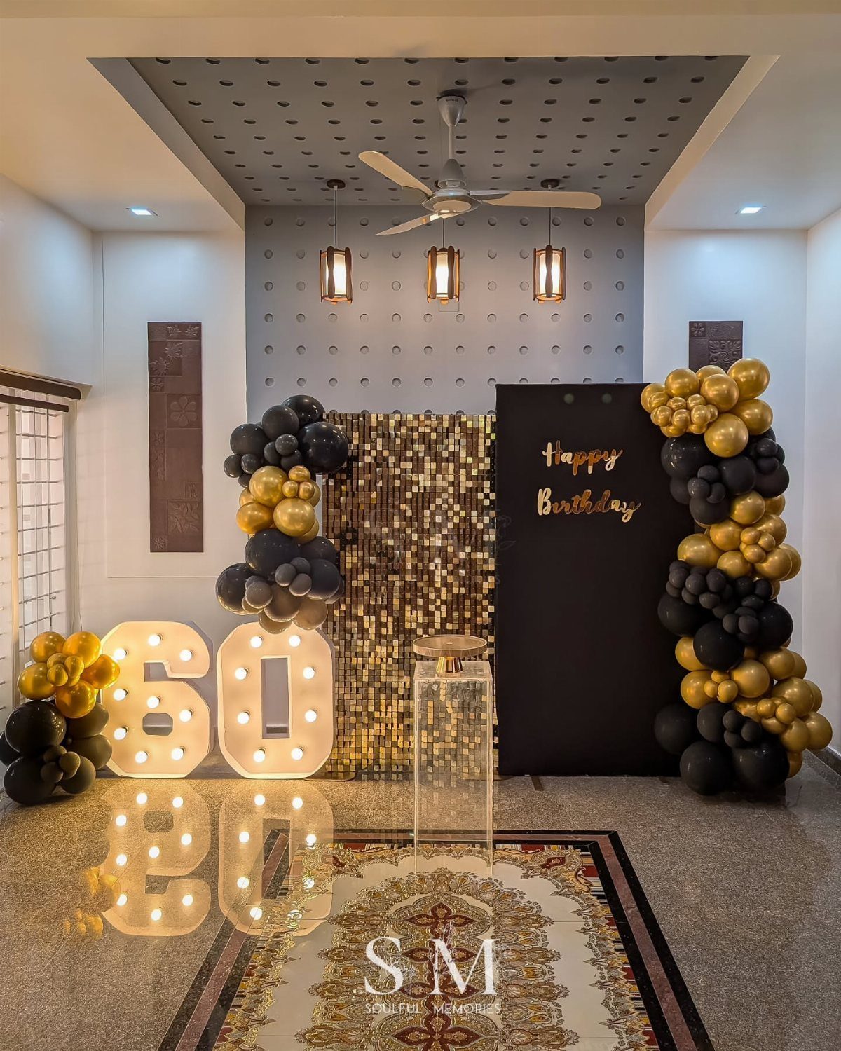 Large illuminated 60 numbers with black and gold balloons and sequin backdrop.