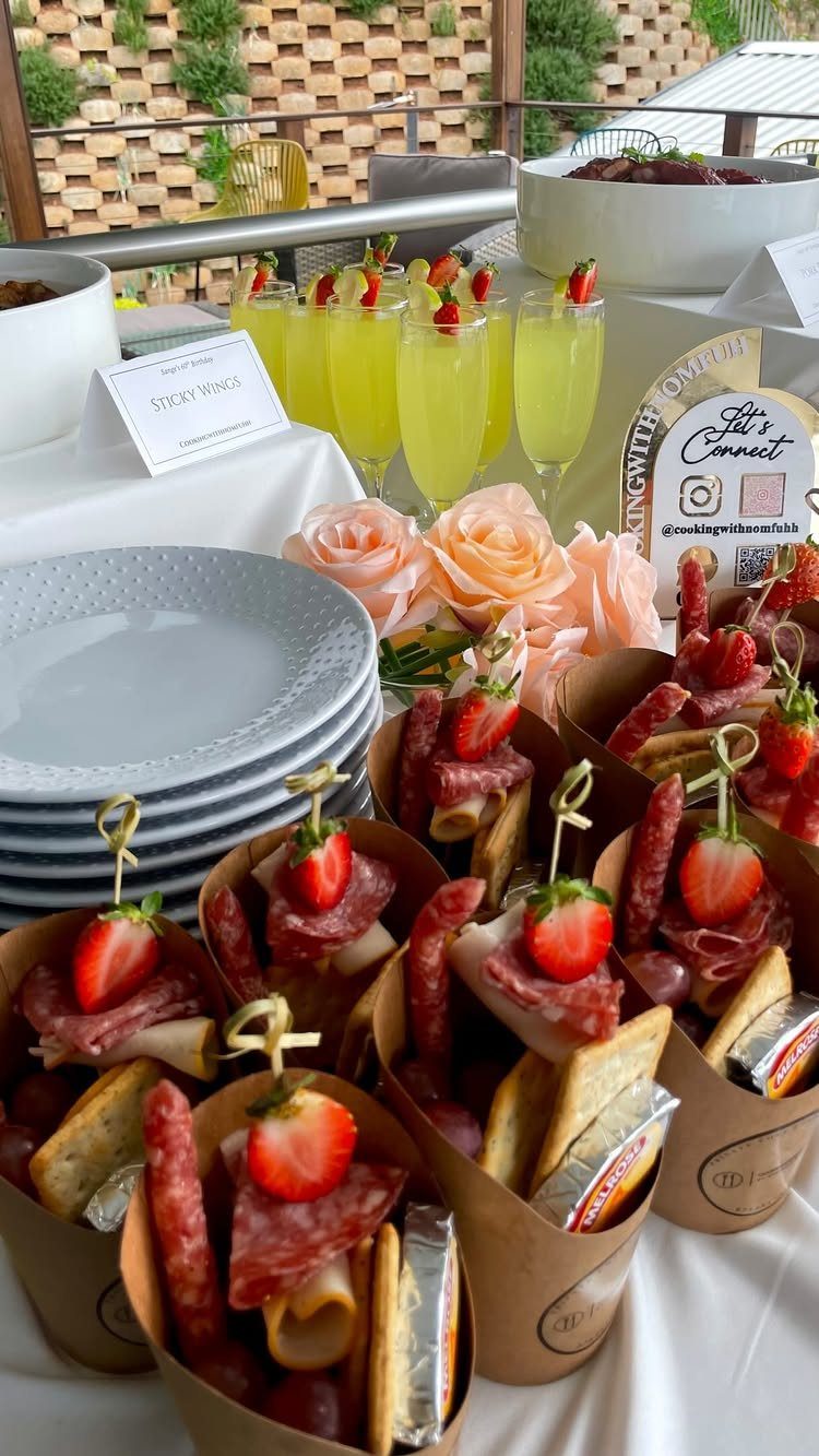 Charcuterie cones and yellow cocktails with strawberries on a white catering table.