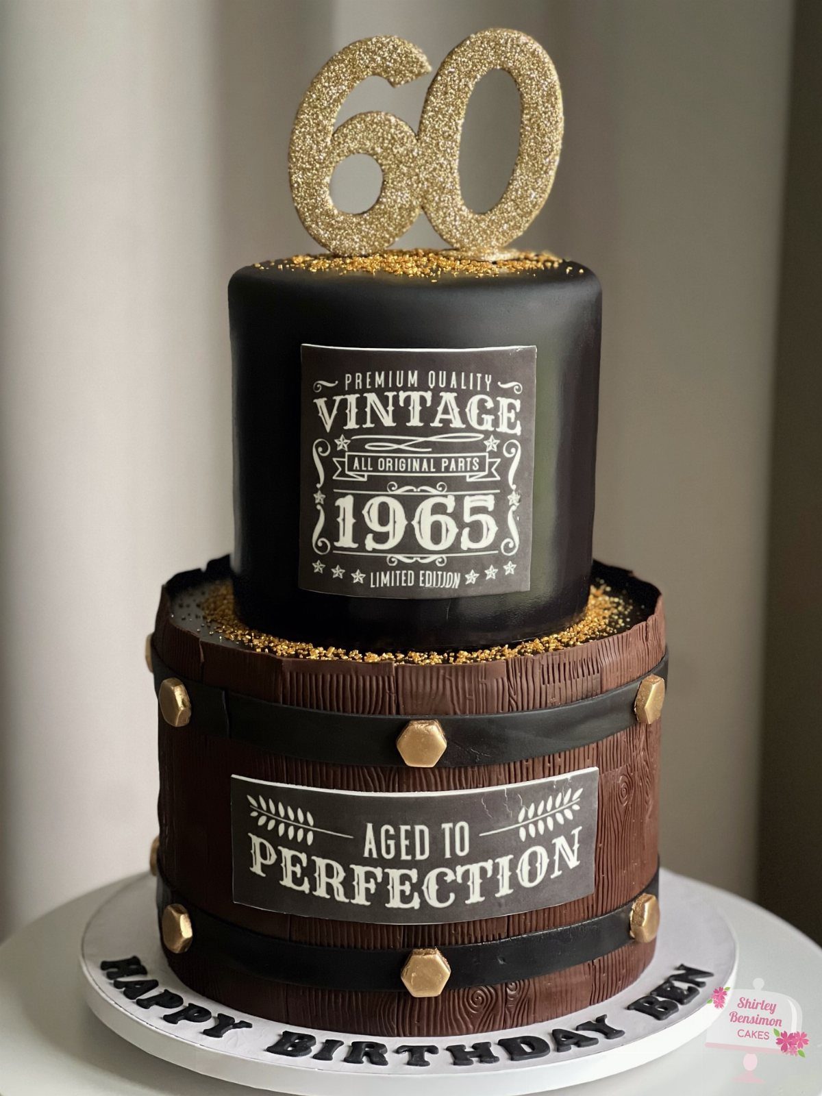 Two-tier birthday cake with a black top and a whiskey barrel bottom tier.