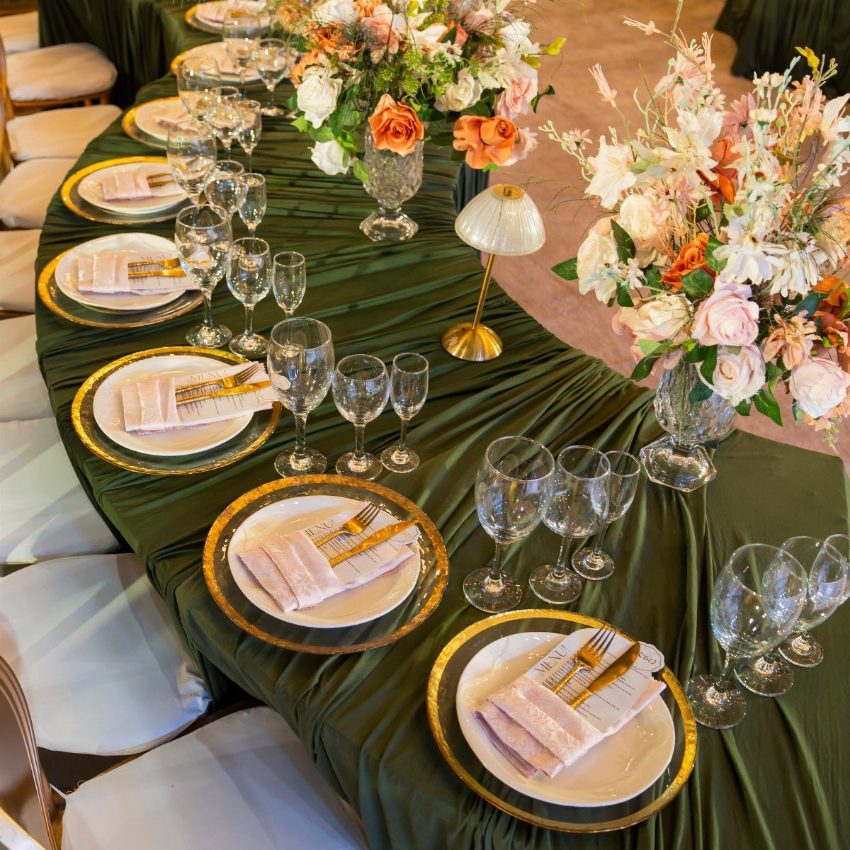 Elegant dinner table setting with green satin cloth, gold plates, and floral centerpieces.