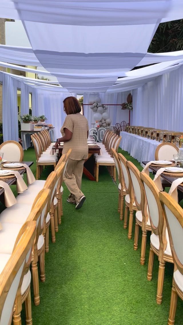 Outdoor dining setup with gold chairs and white canopy on green grass.