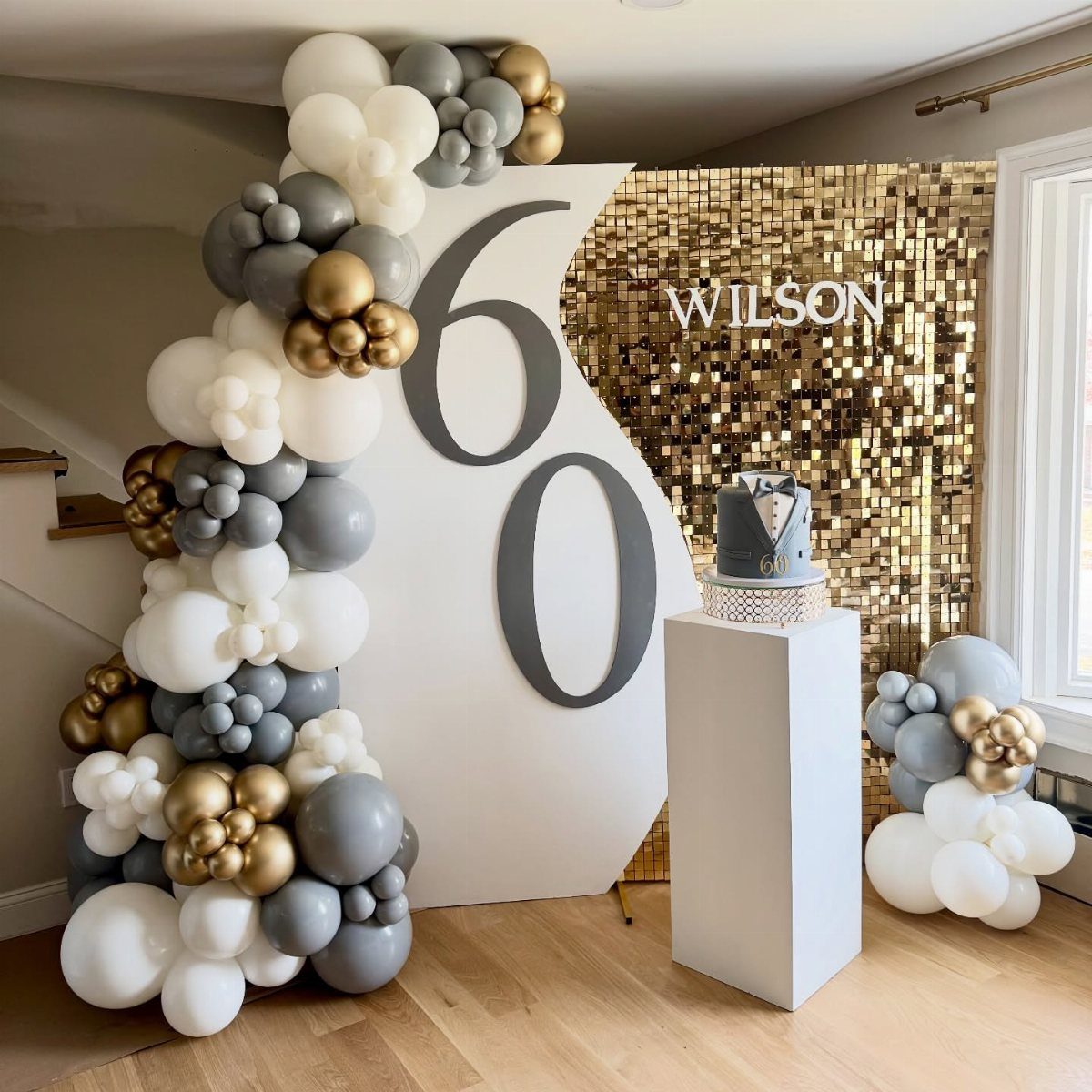 60th birthday party decoration with gold sequins, white backdrop, and balloon arch.