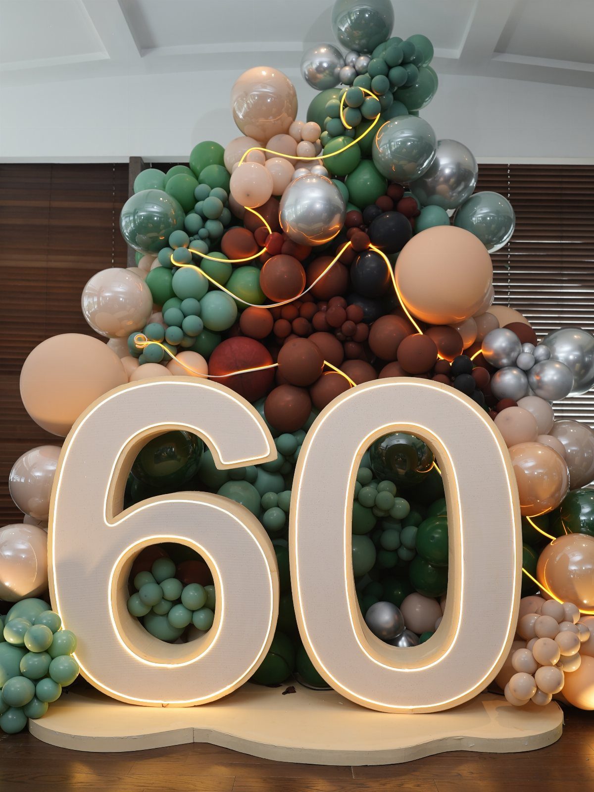 Large glowing number 60 in front of a green and brown balloon arch.