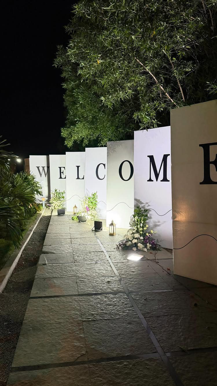 Welcome sign panels with flowers and lanterns along a stone path at night