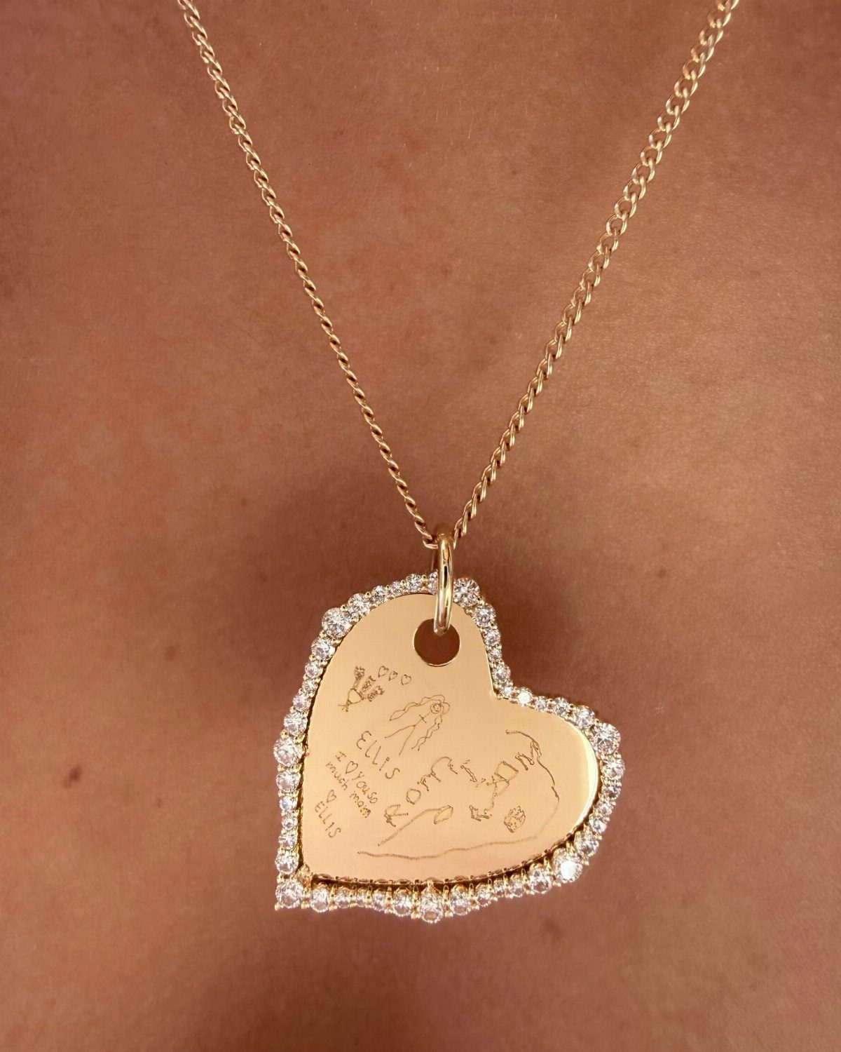 Gold heart-shaped pendant necklace with diamond border and engraved message on a person.