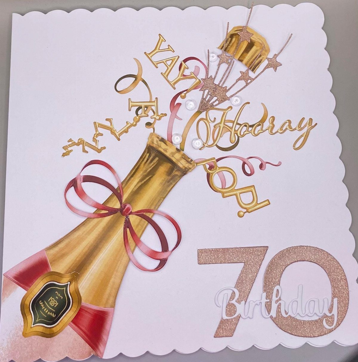 Champagne bottle popping on a white 70th birthday card with gold glitter accents