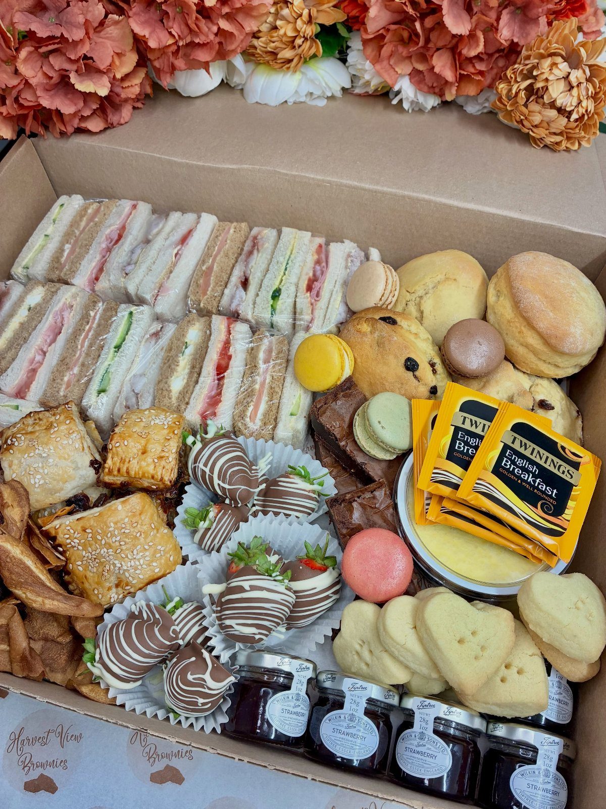 Afternoon tea hamper with sandwiches, scones, sweets, jam, and tea bags in a box.