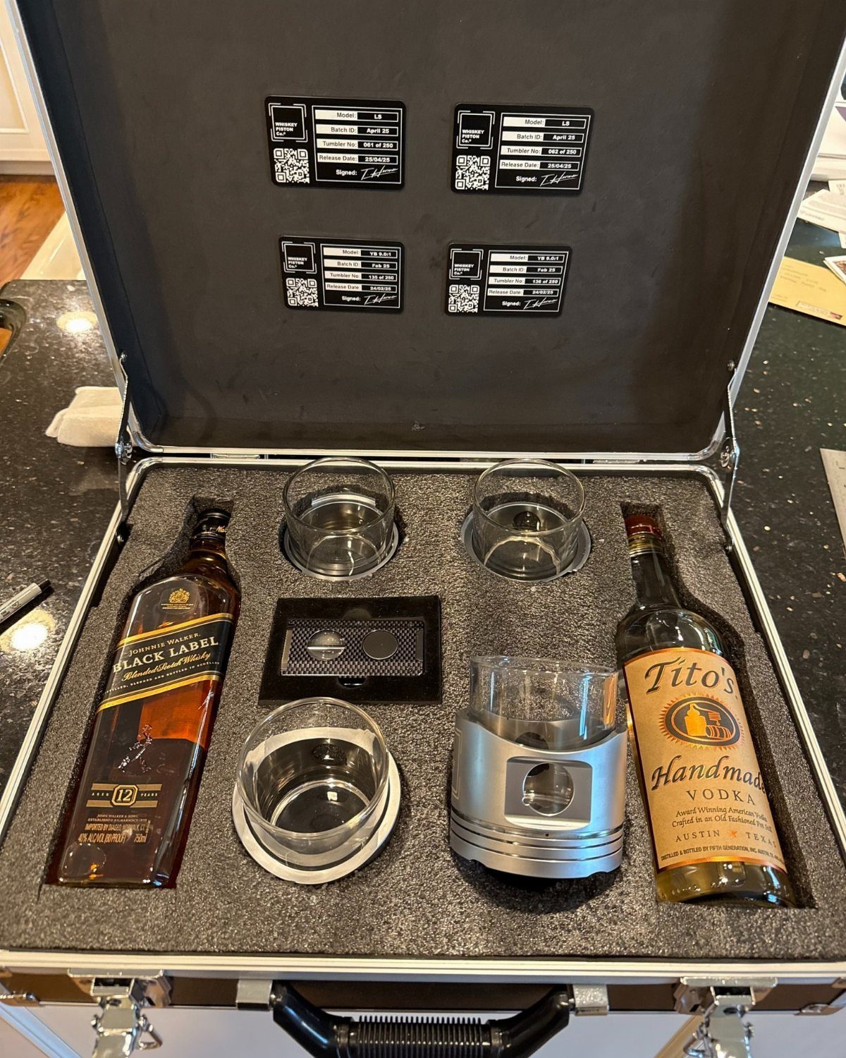 Whiskey and vodka bottles with glasses arranged inside a silver metal briefcase.