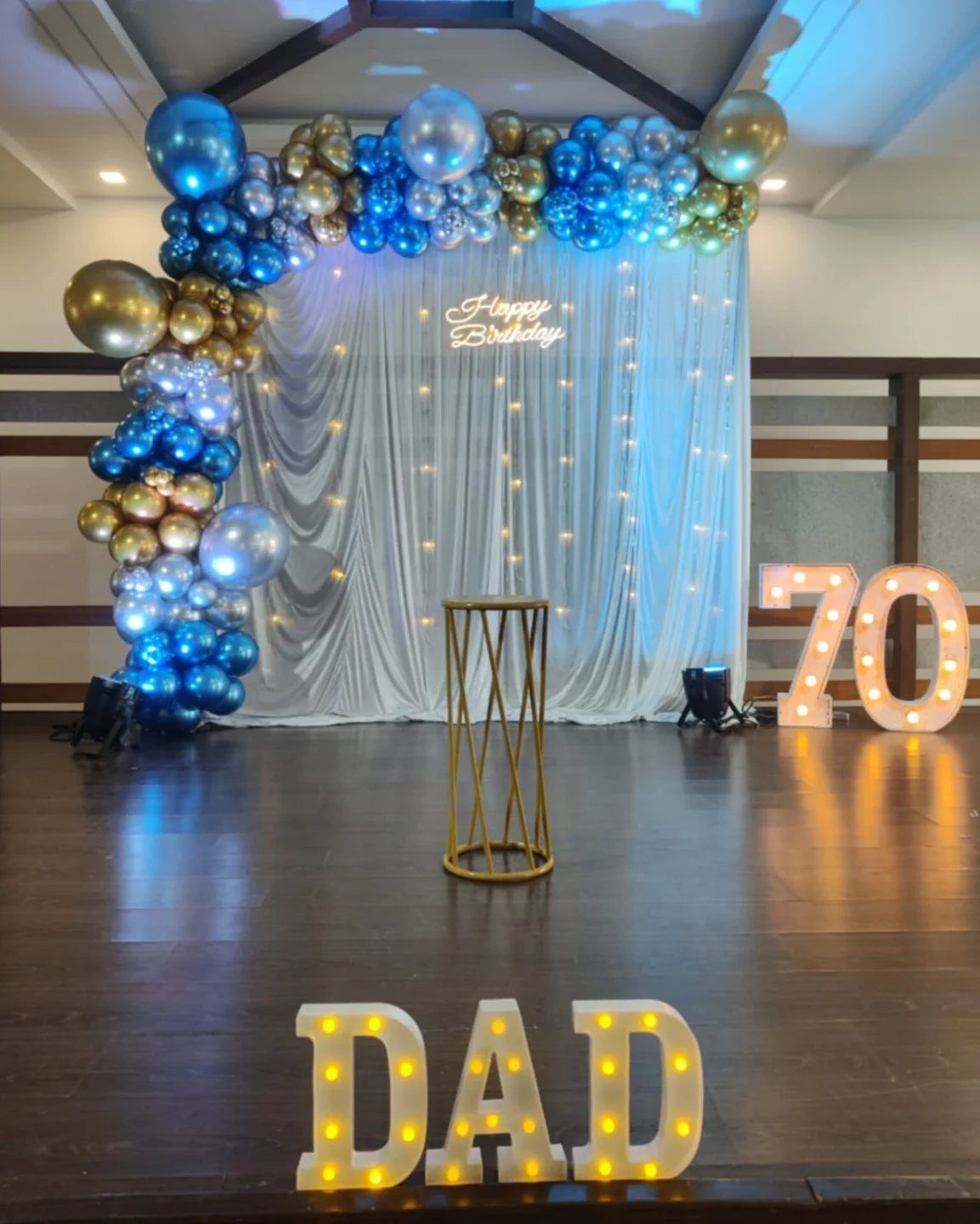 Birthday party decoration with blue and gold balloons and illuminated DAD 70 letters.