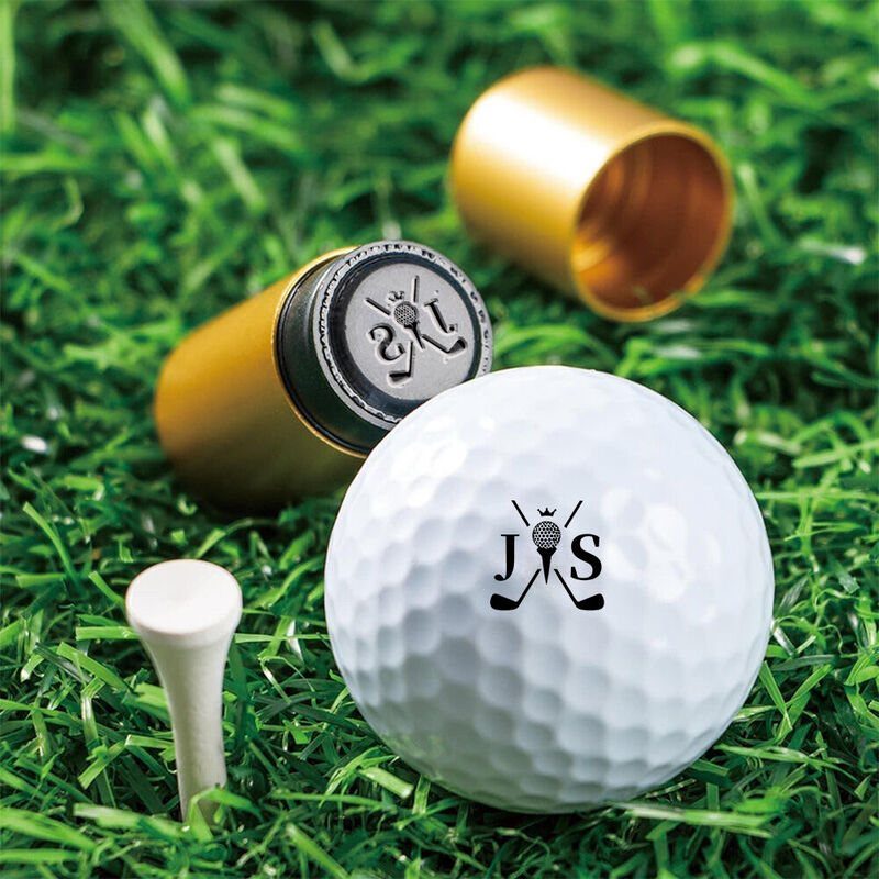 Personalized white golf ball with initials JS on green grass with gold tubes.