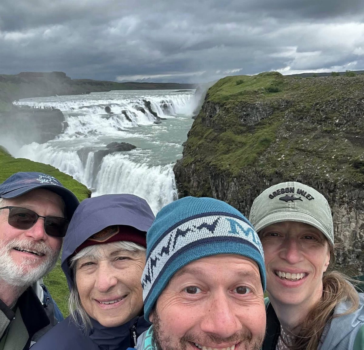 Four smiling adults taking a selfie in front of a massive cascading waterfall.
