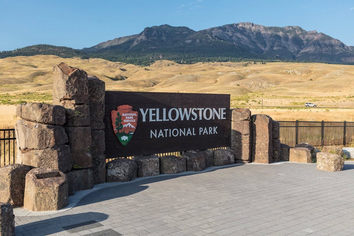 Yellowstone National Park entrance sign with mountains and golden hills in the background