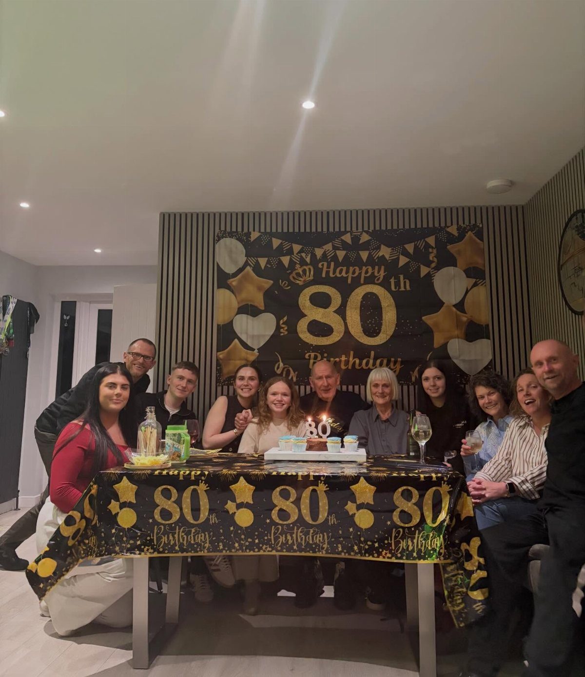 Group of family members posing behind an 80th birthday decorated table and banner.