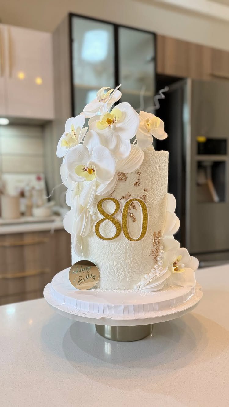 White birthday cake with gold 80 topper and white orchid flowers.