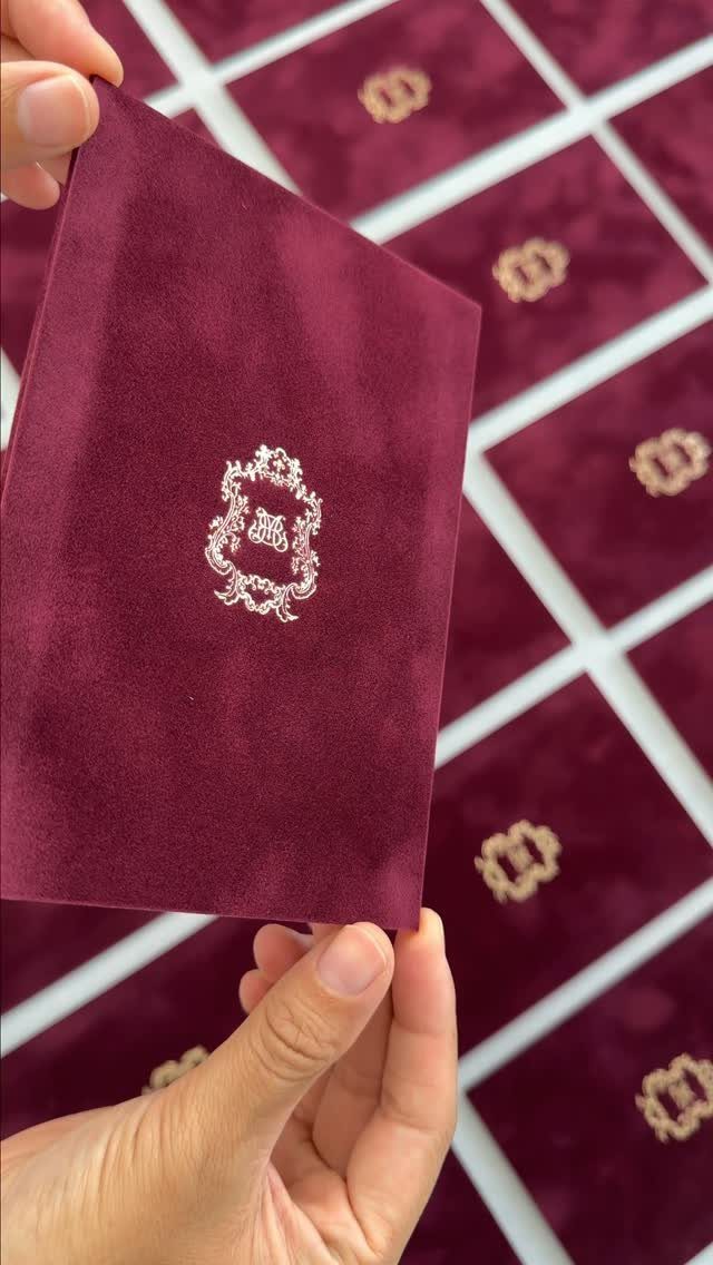 Burgundy velvet invitation card with a silver crest held over similar cards.
