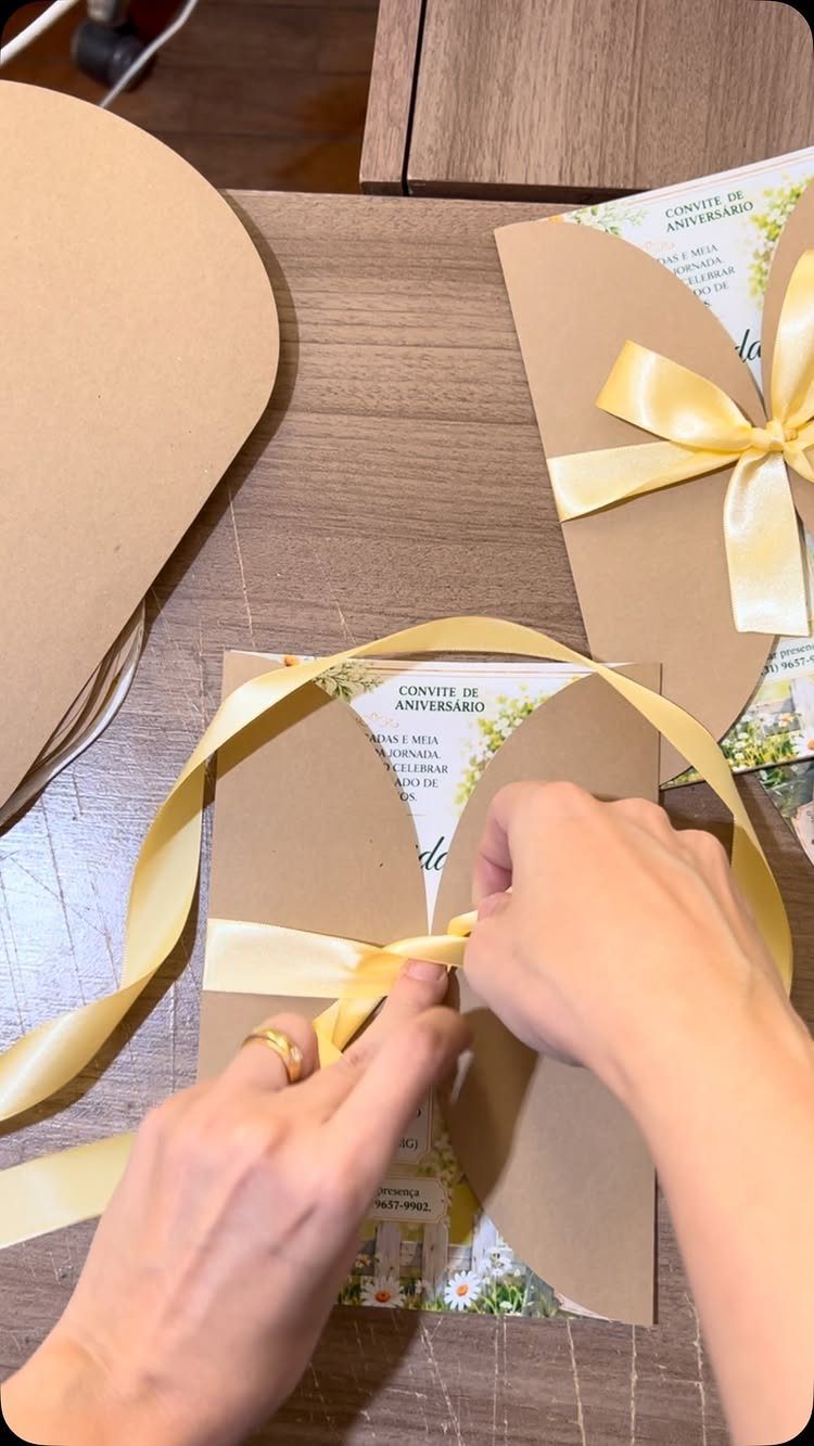Hands tying a yellow ribbon around a floral birthday invitation in a kraft envelope