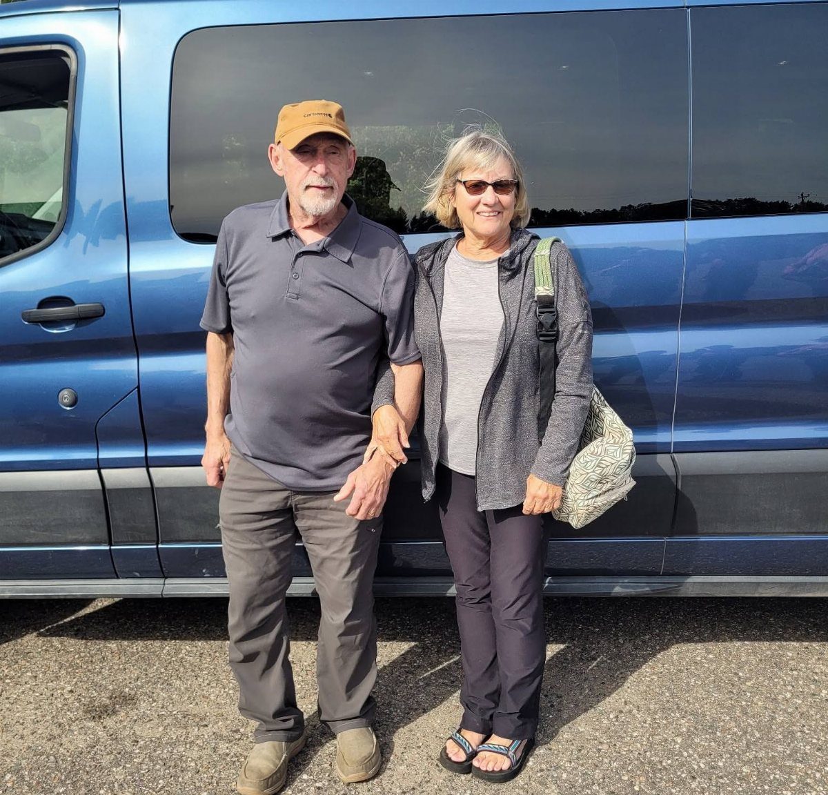 Elderly couple standing in front of a blue van for a trip.