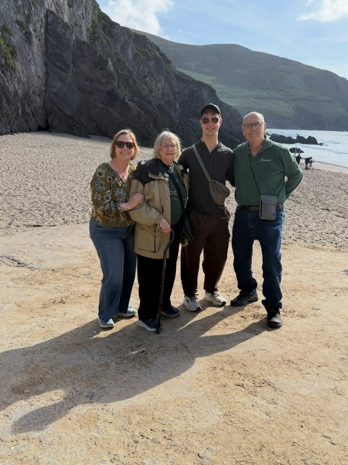 Four family members posing on a sandy beach with steep rocky cliffs behind them.