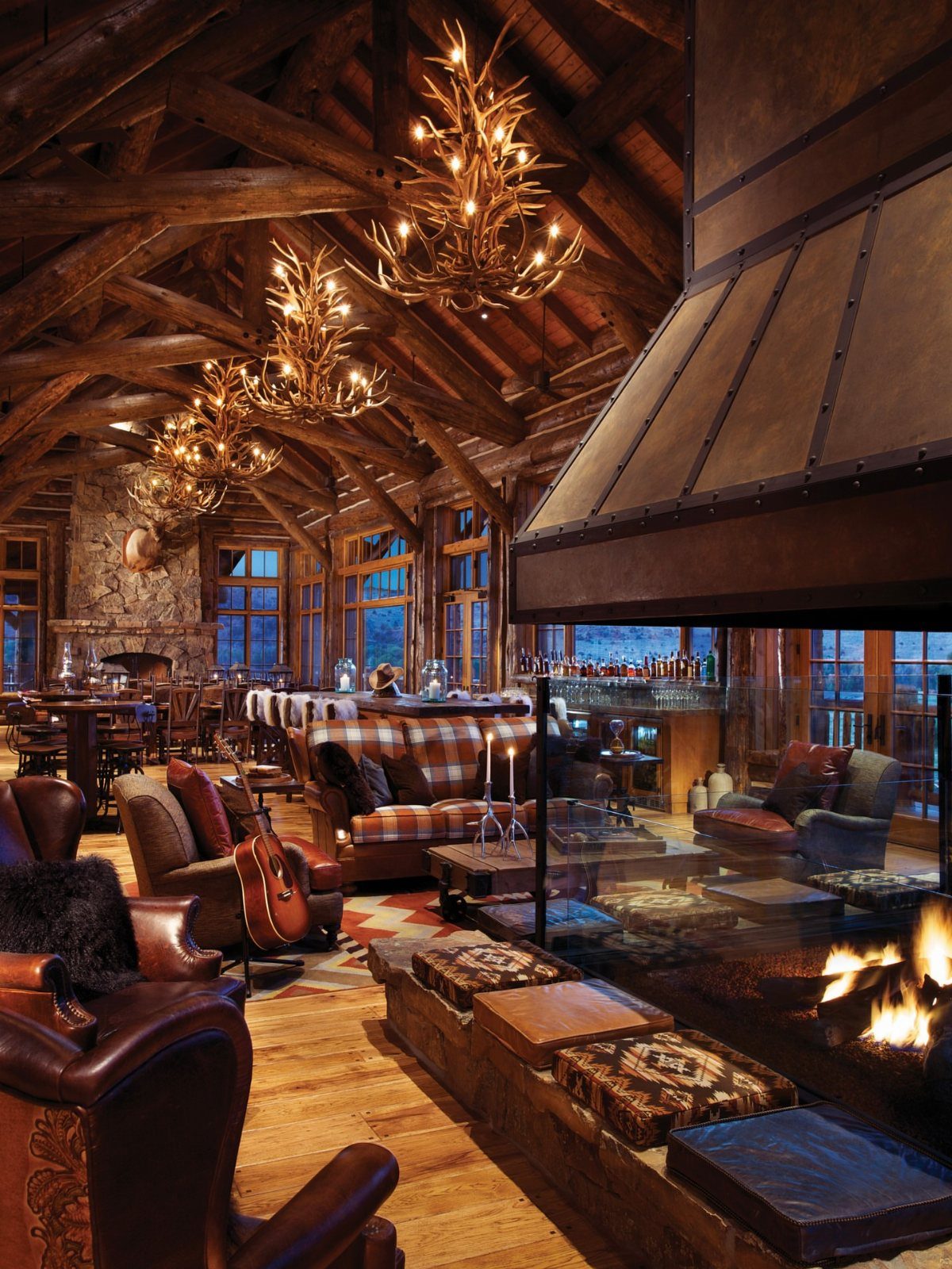 Luxurious rustic lodge interior with antler chandeliers, leather chairs, and a warm fireplace.