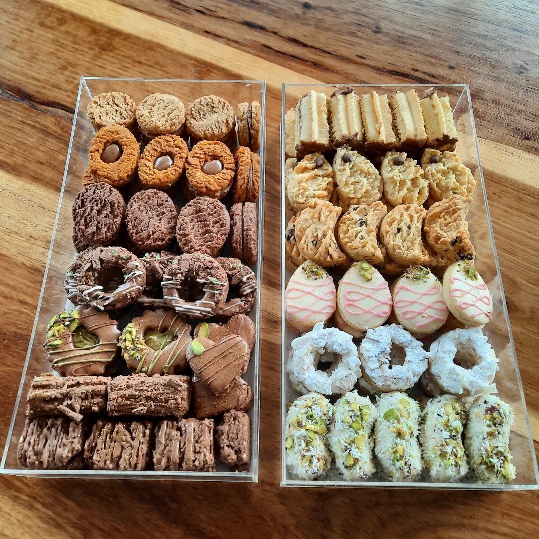 Assorted biscuits and cookies arranged in two clear plastic trays on a wooden table.