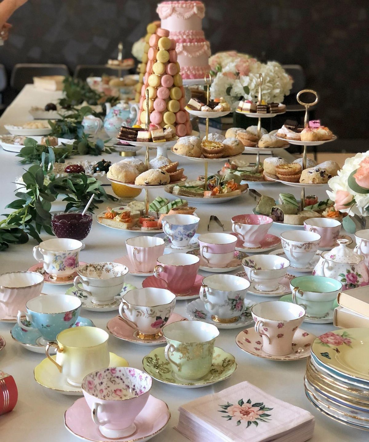Mismatched vintage floral teacups and saucers arranged on a table with tea party treats.