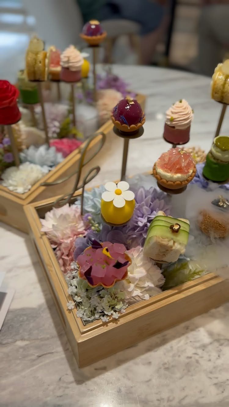 Miniature colorful pastries and cakes arranged with flowers in a wooden tray.