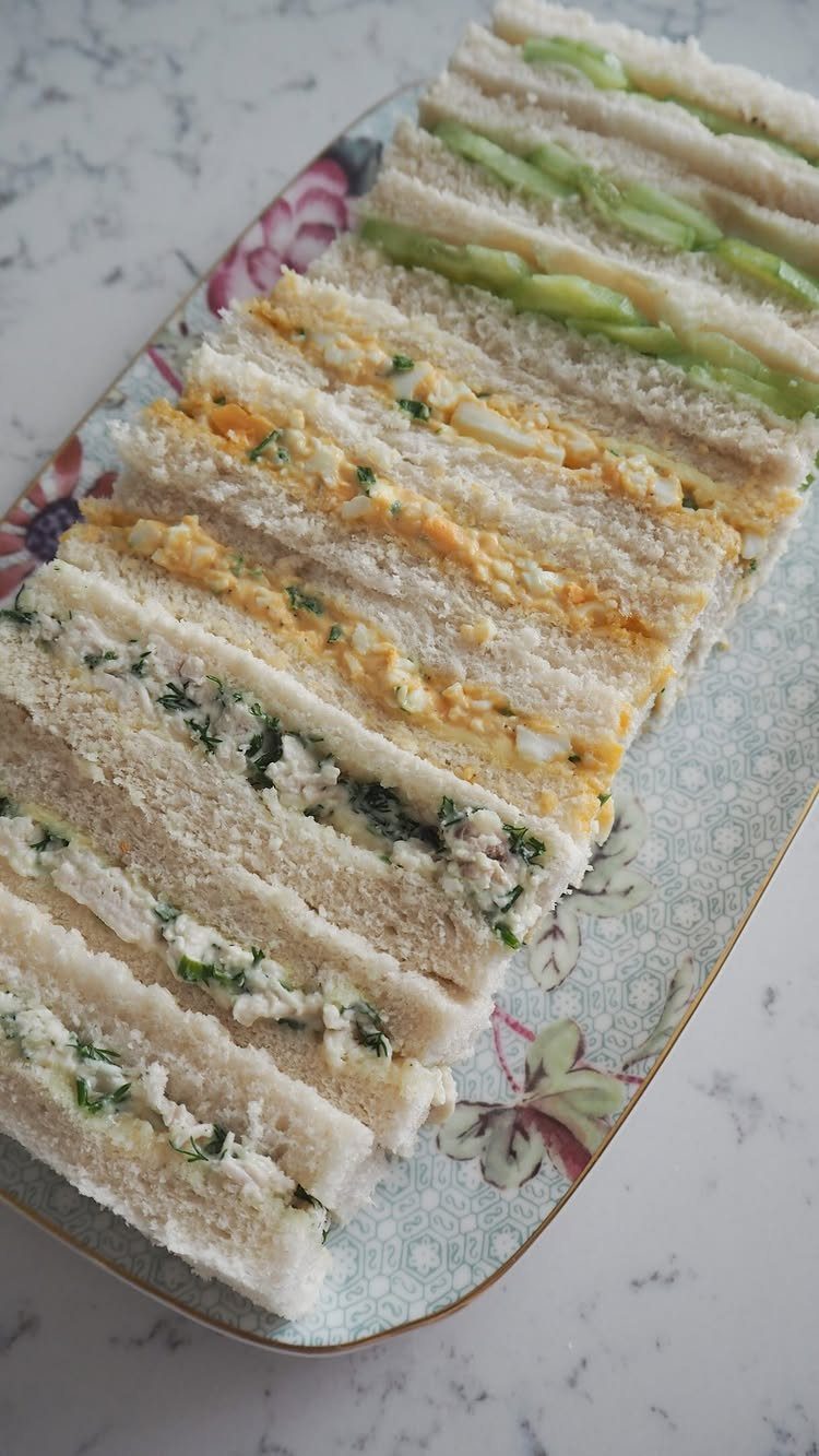 Assorted finger sandwiches with cucumber, egg, and herb fillings on a floral platter.