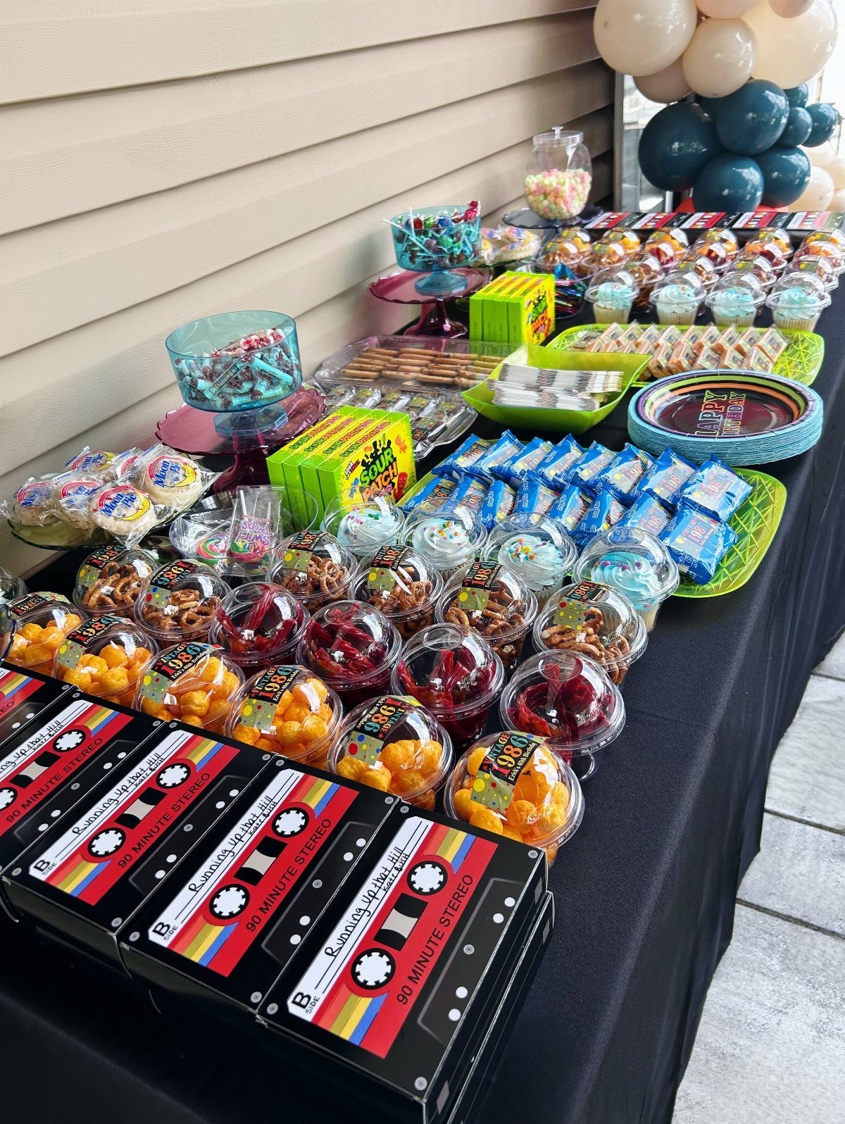 Party dessert table featuring colorful sweets and cassette tape themed treat boxes.