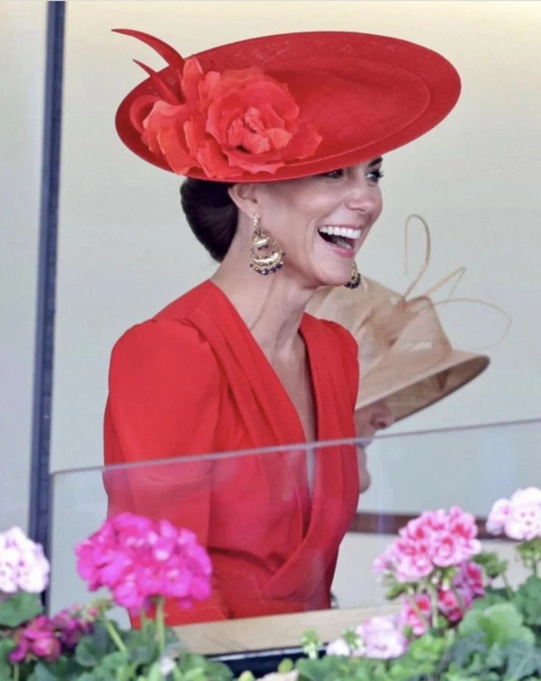 Woman in a red dress and wide-brimmed hat smiling at a racing event.