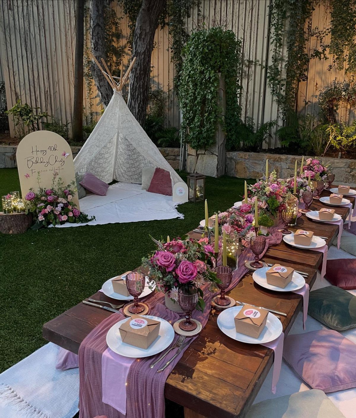 Low wooden table with pink flowers and a white teepee in a garden