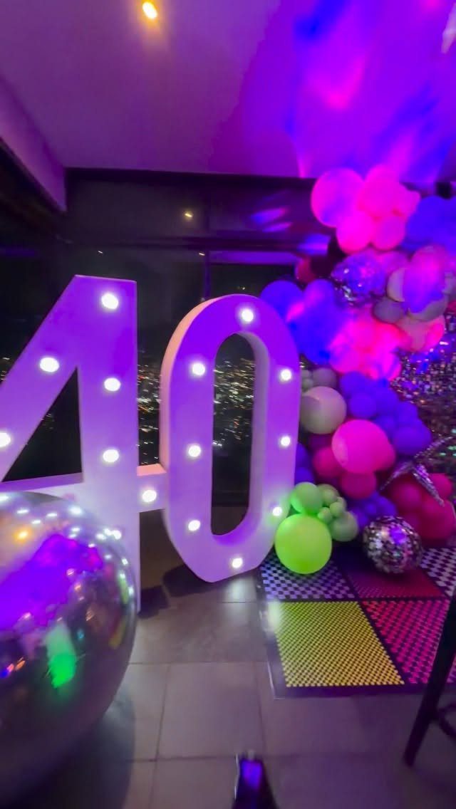 Large illuminated number 40 with colorful balloons and a disco ball at night.
