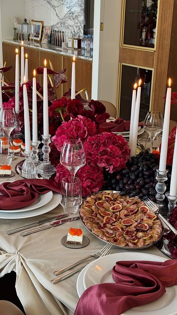 Elegant dining table set with red flowers, white candles, and a fig platter.