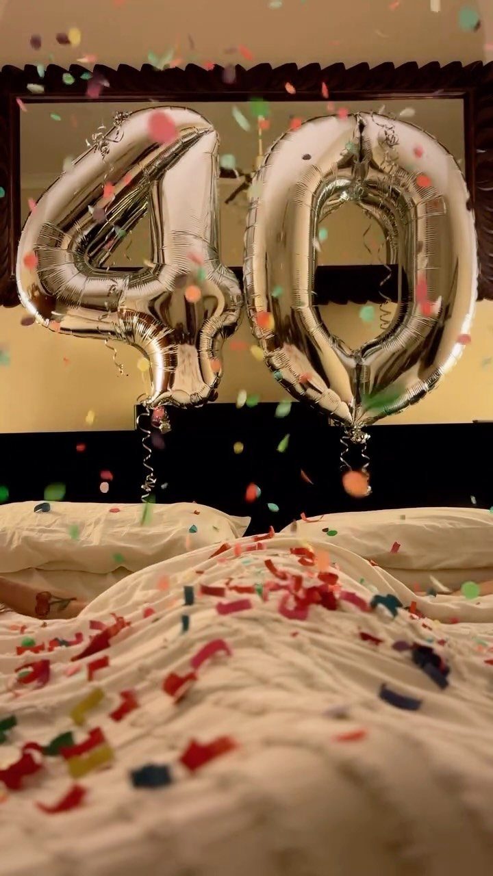 Silver number 40 balloons floating over a white bed with colorful confetti