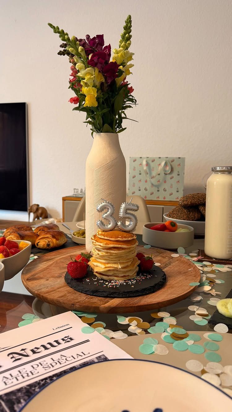 Pancakes with silver 35 balloons, flowers, and breakfast foods on a festive table.