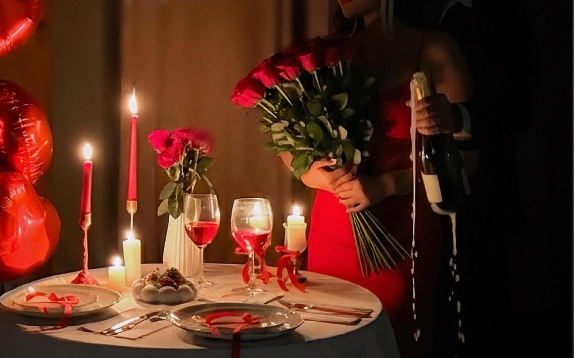 Woman in red dress holding roses and champagne at a candlelit dinner table